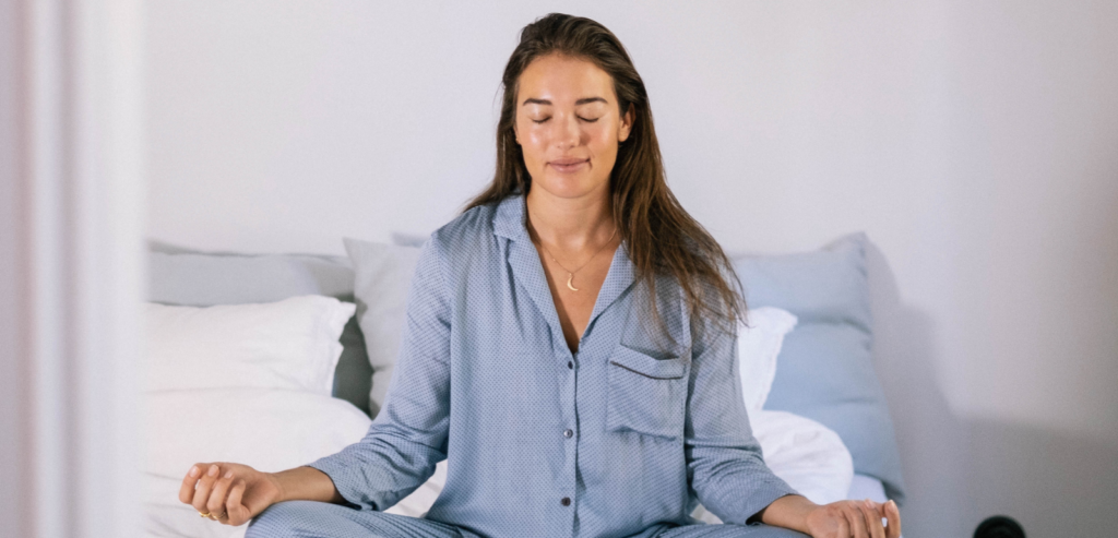 En kvinna mediterar i sängen med korslagda ben