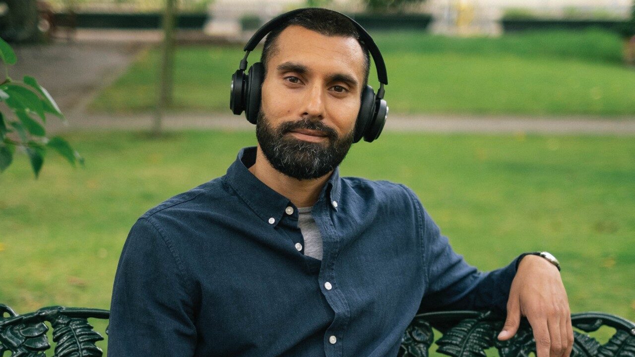 man ler mot kameran på en bänk i det gröna med app i handen